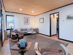 A modern living room with a sofa, coffee table, and chairs, a rug, and a framed picture on the wall.