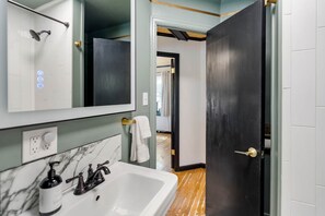 A bathroom with a white sink, a mirror, a shower, and a towel rack. - Stylish 1Br Near Main St | The Troubadour Suite (Sheridan)