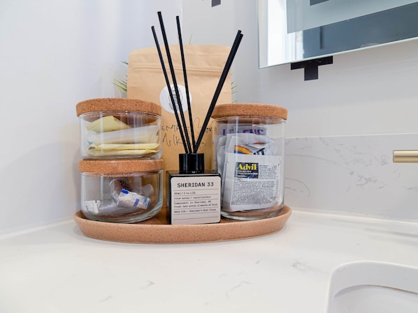 A kitchen counter with three glass jars with cork lids, a bottle of Advil, and a bottle of room spray.