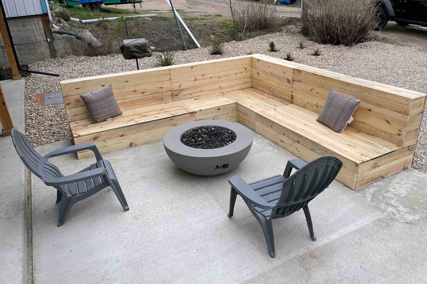 A concrete patio with a wooden bench seating area, two chairs, and a circular fire pit.