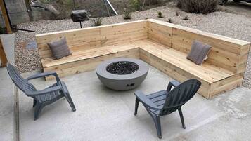 A concrete patio with a wooden bench seating area, two chairs, and a circular fire pit.