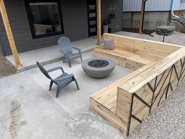 An outdoor seating area with a fire pit, two chairs, and a wooden bench.