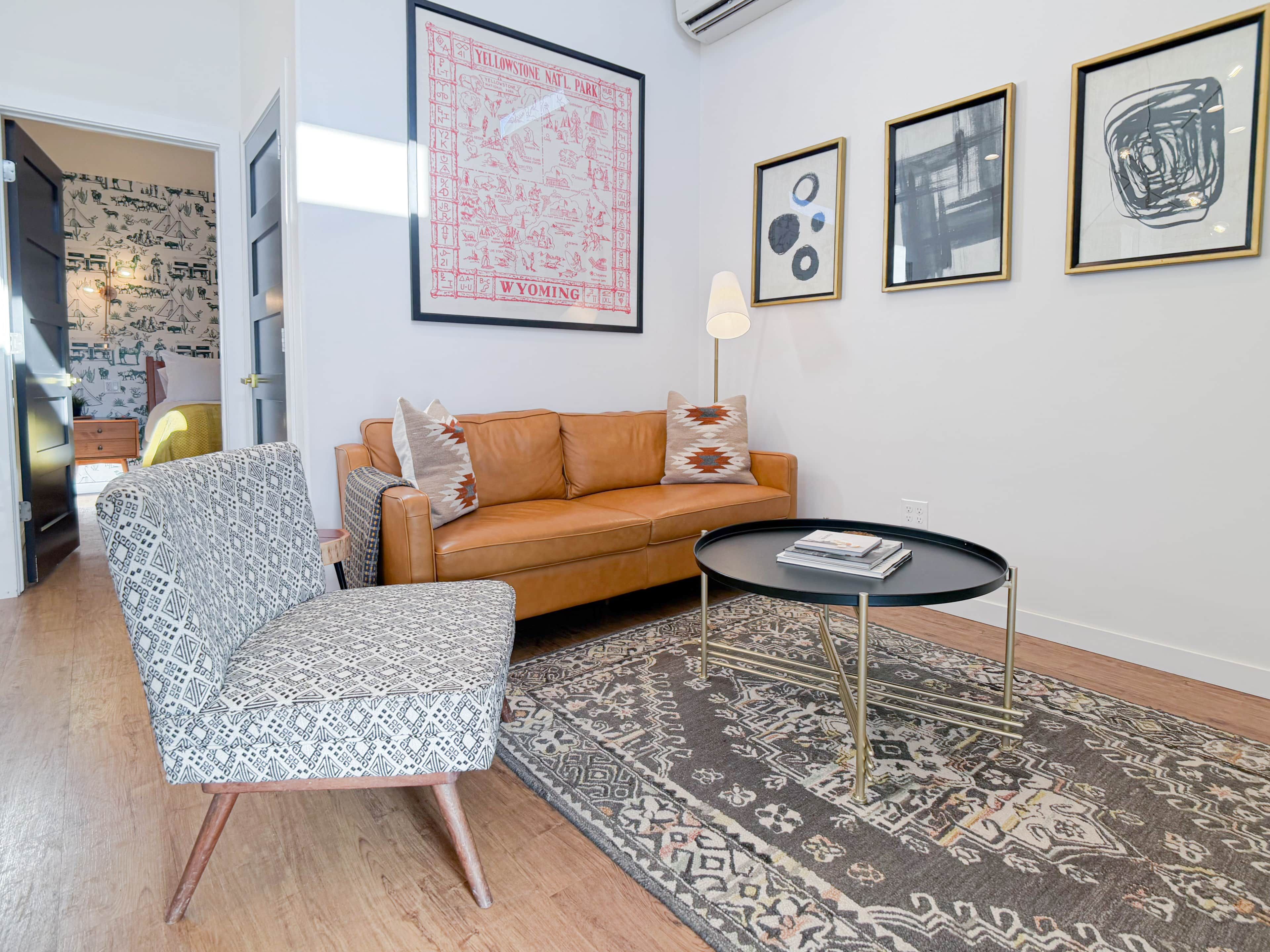 A living room with a sofa, patterned armchair, a coffee table, and a rug. There are framed pictures on the wall.