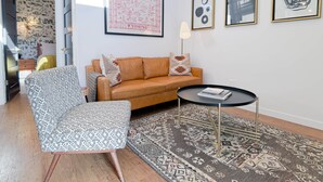 Una sala de estar con un sofá, un sillón estampado, una mesa de centro y una alfombra. Hay cuadros enmarcados en la pared.