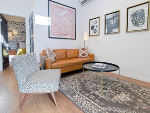 Una sala de estar con un sofá, un sillón estampado, una mesa de centro y una alfombra. Hay cuadros enmarcados en la pared.