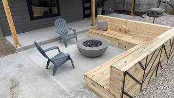 An outdoor seating area with a fire pit, two chairs, and a wooden bench.