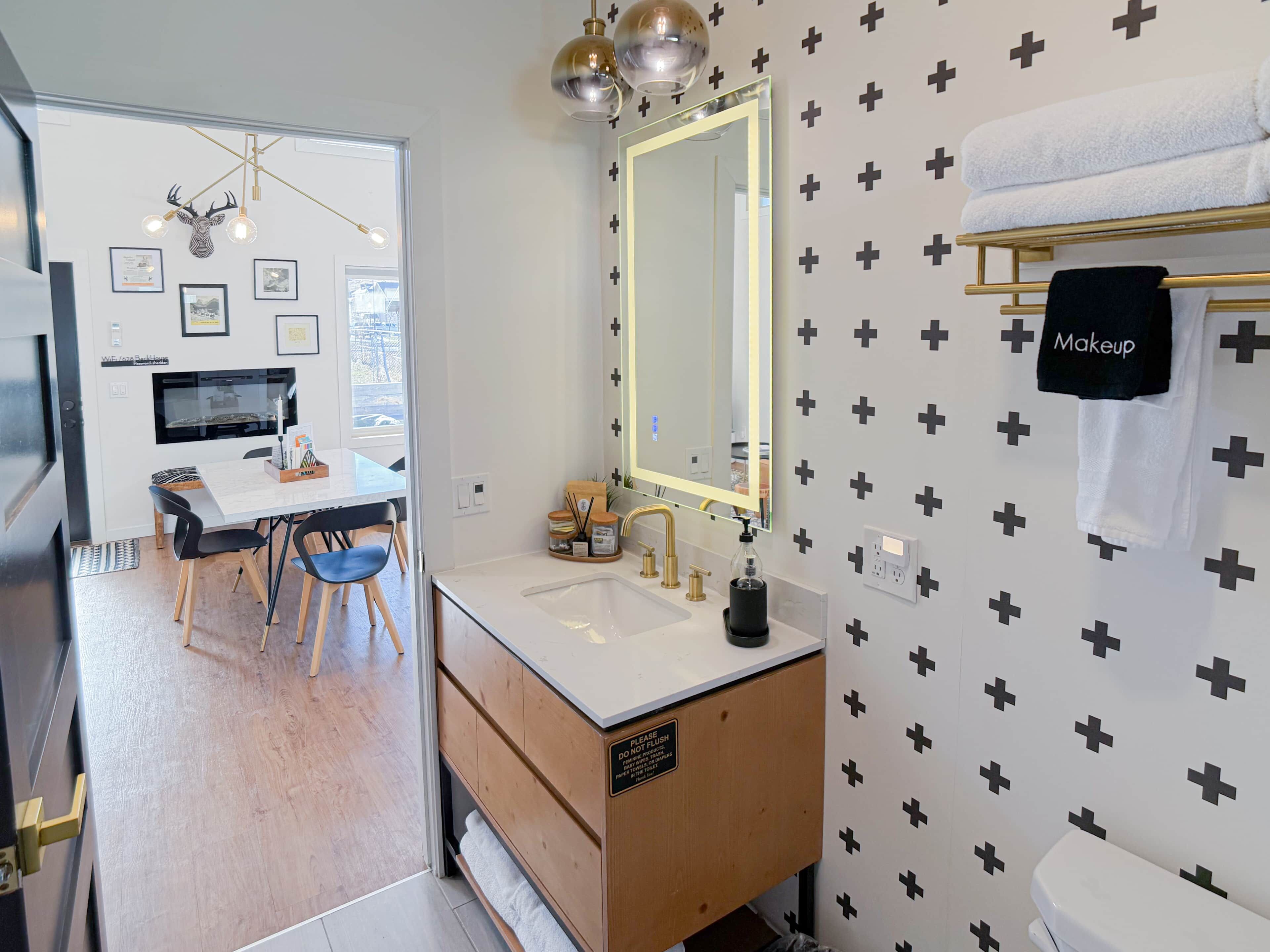 Une salle de bain moderne avec un grand miroir, un lavabo et des toilettes. On y trouve un meuble-lavabo avec un porte-serviettes et un panneau indiquant qu’il ne faut pas tirer la chasse d’eau.