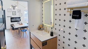 Une salle de bain moderne avec un grand miroir, un lavabo et des toilettes. On y trouve un meuble-lavabo avec un porte-serviettes et un panneau indiquant qu’il ne faut pas tirer la chasse d’eau.