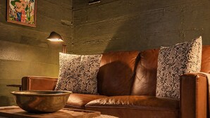 Eine braune Ledersofa mit floralen Kissen, eine Holzschale auf einem Tablett und eine Wandlampe.