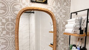 Ein Badezimmer mit einem großen Spiegel, einem weißen Waschbecken und einem Ablagefach mit Pflegeprodukten.