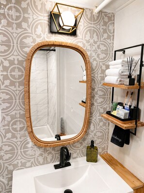Une salle de bain avec un grand miroir, un lavabo blanc et une étagère contenant des articles de toilette.