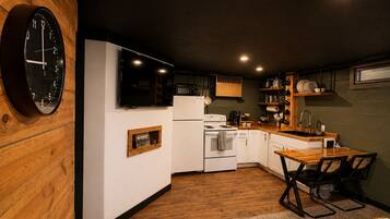A kitchen with a clock, white cabinets, a stove, and a dining area with chairs.
