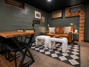 Une pièce comprenant une table à manger en bois, deux bancs rembourrés, un canapé en cuir avec des coussins à motifs, une petite table d’appoint et un tapis à carreaux.