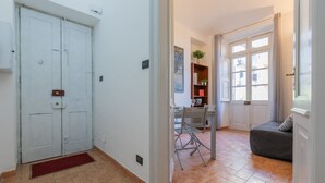 Ein Flur mit geschlossener Tür, ein Essbereich mit Tisch und Stühlen sowie ein Sofa in einem Zimmer mit Fenster.