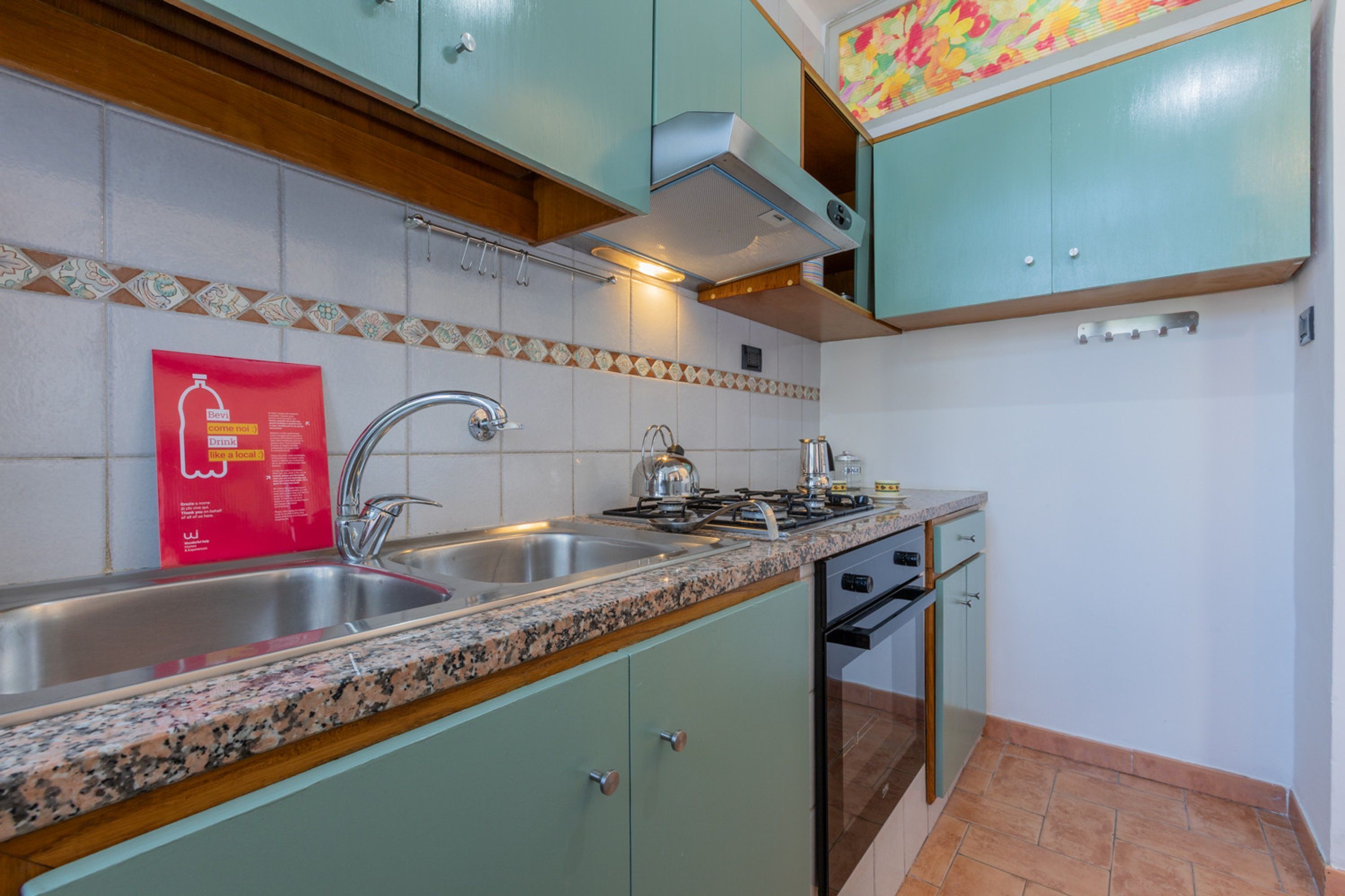 A kitchen with granite countertops, stainless steel sink, and teal cabinets.