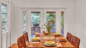 A dining area with a wooden table set for four, surrounded by white walls and doors leading to a garden. - 4br/2ba Zen Garden mins to adventures (Stuart)