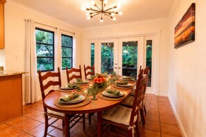 A dining area with a wooden table set for four, surrounded by chairs, with a view of greenery through the windows. - 4br/2ba Zen Garden mins to adventures (Stuart)
