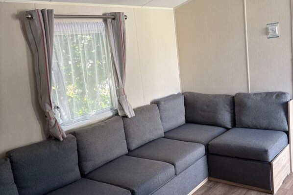 A corner sofa with a window and curtains. - Seaside Lodge Haven in St Osyth (Clacton-on-Sea)