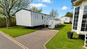 A caravan park with a paved driveway leading to a caravan, a grassy lawn, and a white building with large windows.