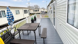 Une terrasse avec des tables et des chaises pour pique-nique, un parasol bleu et une clôture blanche.