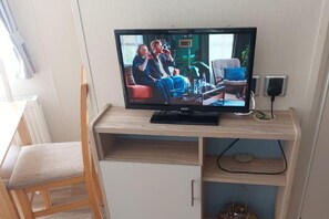A television on a wooden TV stand in a room with a white cabinet below. - Seaside Lodge Haven in St Osyth (Clacton-on-Sea)