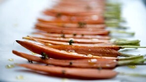 A row of sliced carrots with olive oil and herbs on a white surface.