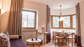 Une pièce chaleureuse avec un canapé, une petite table ronde en verre et un coin repas comprenant des chaises et une table.