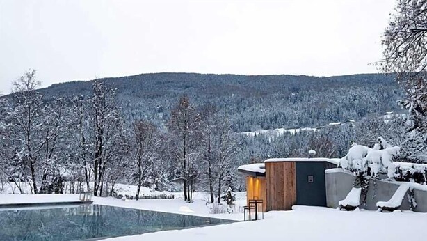 Ein modernes Haus mit Swimmingpool, umgeben von schneebedeckten Bäumen und Hügeln.
