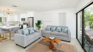 Een moderne woonkamer met een grijze bank, een salontafel en een eethoek met een witte tafel en stoelen.
