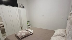 Un dormitorio con cama, armario blanco y una mesita con una planta.