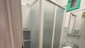 Un baño con cabina de ducha, lavabo y un ventanal pequeño.