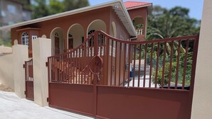 A gated entrance with a red metal gate and a staircase leading to a building with arched windows and a red roof. - Beautiful 3-bedroom house with Oceanview in Hope Bay and AC (Hope Bay)