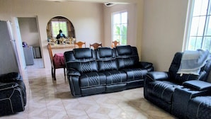A spacious living room with a black leather sofa, a dining table with chairs, and a ceiling fan. - Beautiful 3-bedroom house with Oceanview in Hope Bay and AC (Hope Bay)