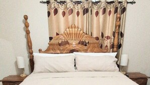 A neatly made bed with a wooden headboard, white linens, and a towel with a tag on it. There are two bedside tables with lamps and a window with curtains. - Beautiful 3-bedroom house with Oceanview in Hope Bay and AC (Hope Bay)