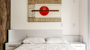 A bedroom with a bed, two bedside tables, a wall-mounted artwork, and a wooden panel on the left.