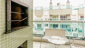 A balcony with a grill, wicker chairs, and a view of neighboring buildings.
