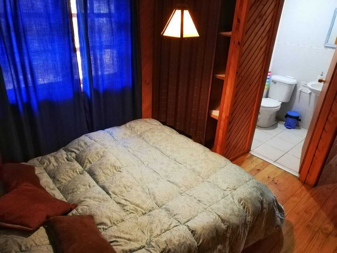 Una camera da letto con un letto, una porta in legno e un bagno visibile attraverso una porta aperta.