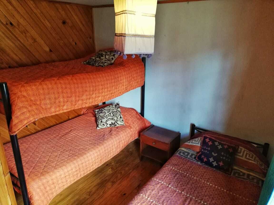 Een kamer met twee stapelbedden, een klein houten nachtkastje en een raam met gordijn.