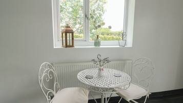 A white metal table with two chairs, a white radiator below, and a window with a view of greenery.