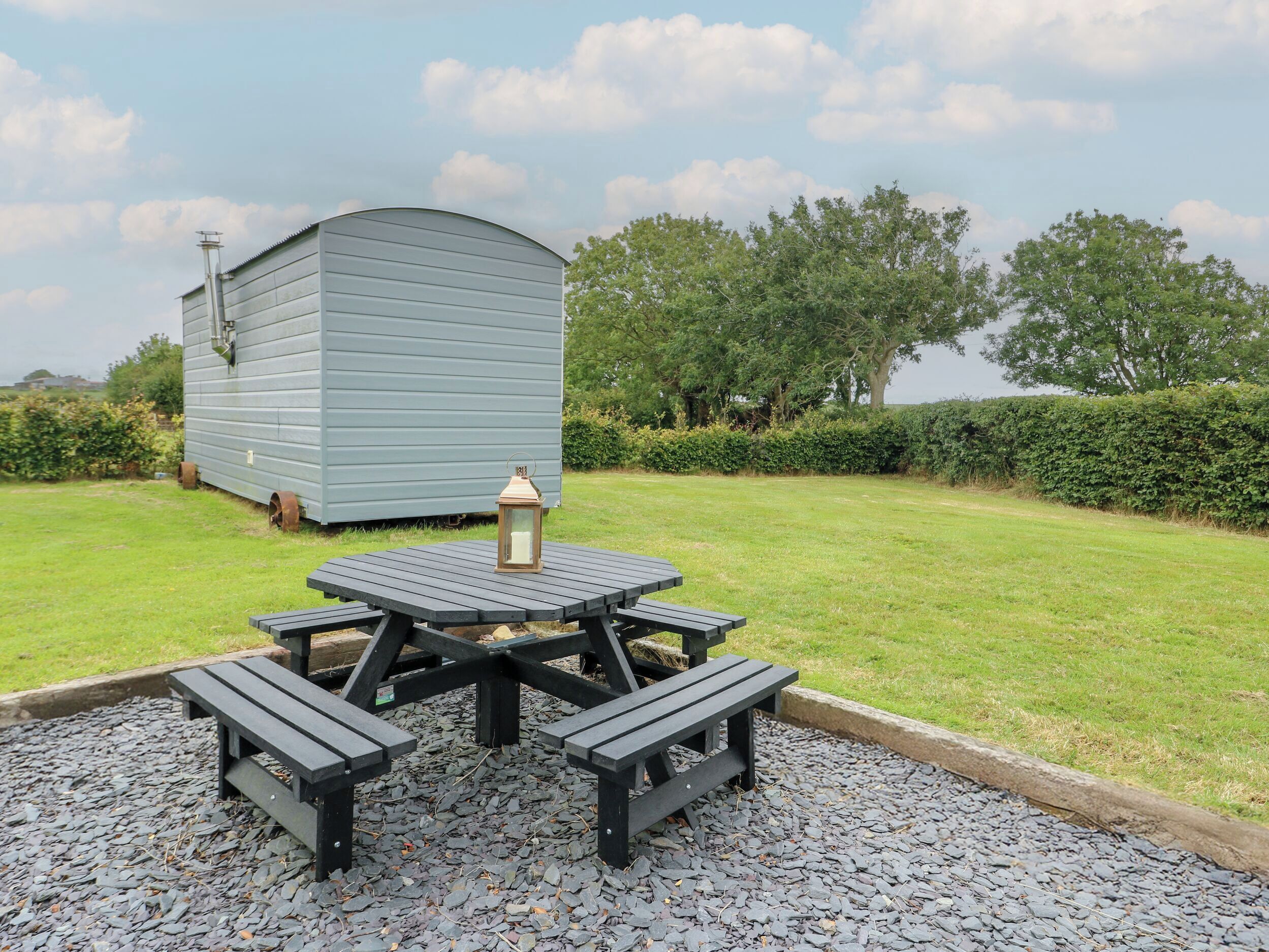 A picnic table with benches and a lantern in a grassy area with a shed in the background.