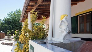 Un edificio con fachada blanca, una estatua y un jardín con plantas de flores amarillas.