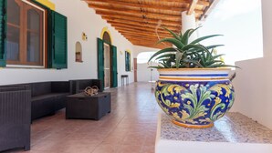 Amplio espacio interior con techo de madera, una maceta decorativa grande con una planta y una zona de estar con un sofá y una mesita.