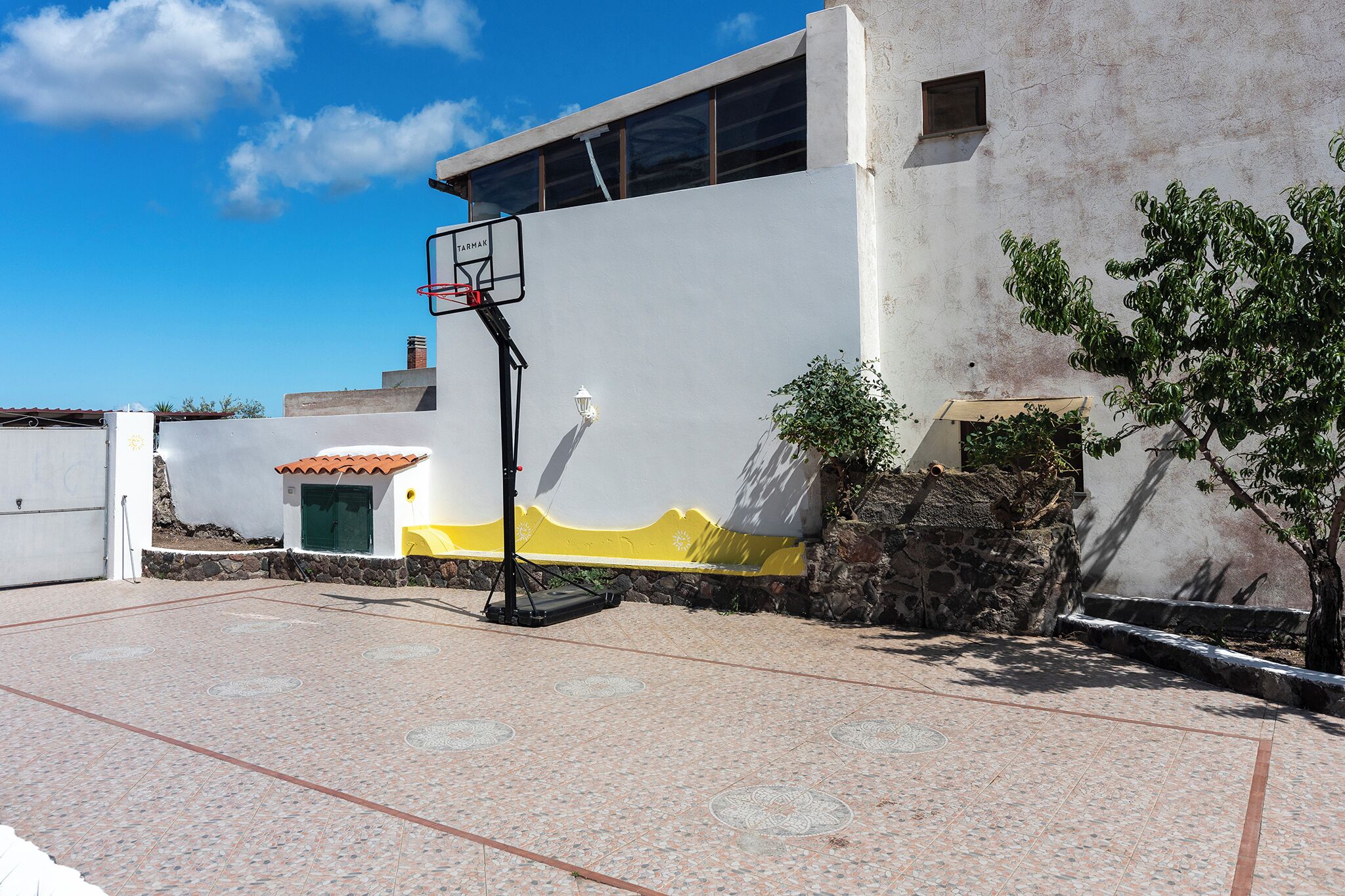 A basketball court with a hoop, a small shed, and a stone wall.