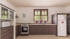 Eine kleine Küche mit Mikrowelle, Backofen, Kühlschrank und einem Fenster mit dekorativen Fliesen.