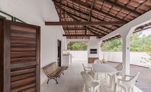 Une terrasse couverte avec un banc en bois, des chaises en plastique blanc et une table.