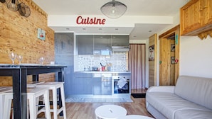 A modern kitchen with stainless steel appliances, a dining area with stools, and a living room with a sofa.