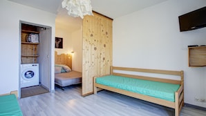 A small, clean room with a wooden bed, a washing machine, and a wooden wardrobe.