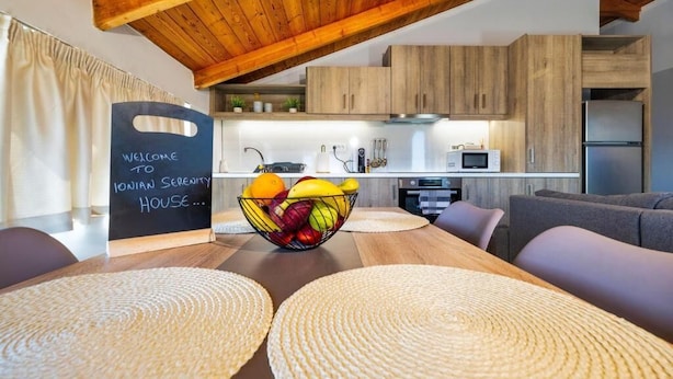 A modern kitchen with wooden cabinets, a blackboard sign, and a fruit bowl on the table. - Ionian Serenity House (Zakynthos)