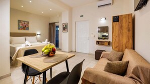 A modern hotel room with a bed, a dining area with a fruit bowl, a sofa, and a wooden accent wall. - Ionian Serenity House (Zakynthos)