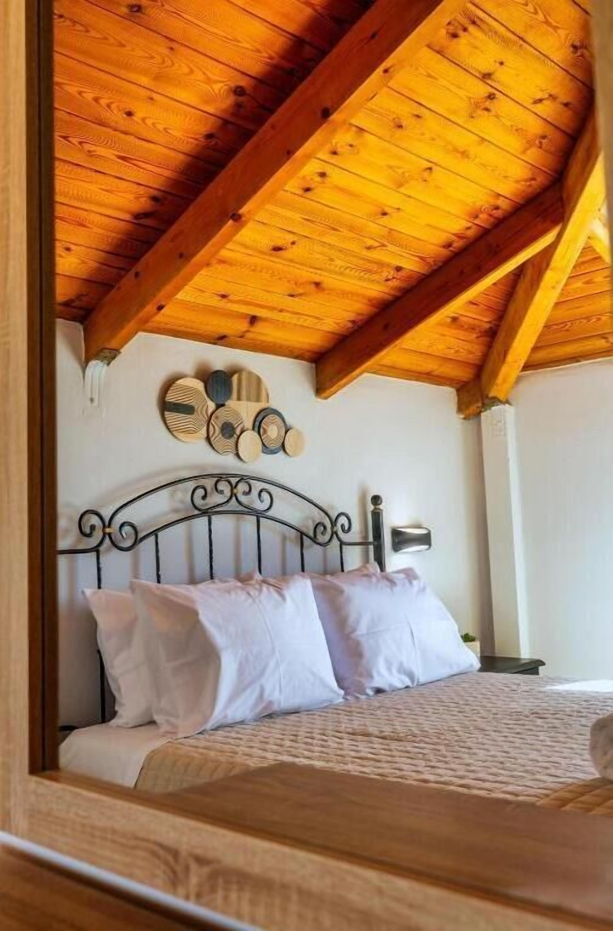 Une chambre avec un plafond en bois, un cadre de lit en métal et un luminaire fixé au mur.